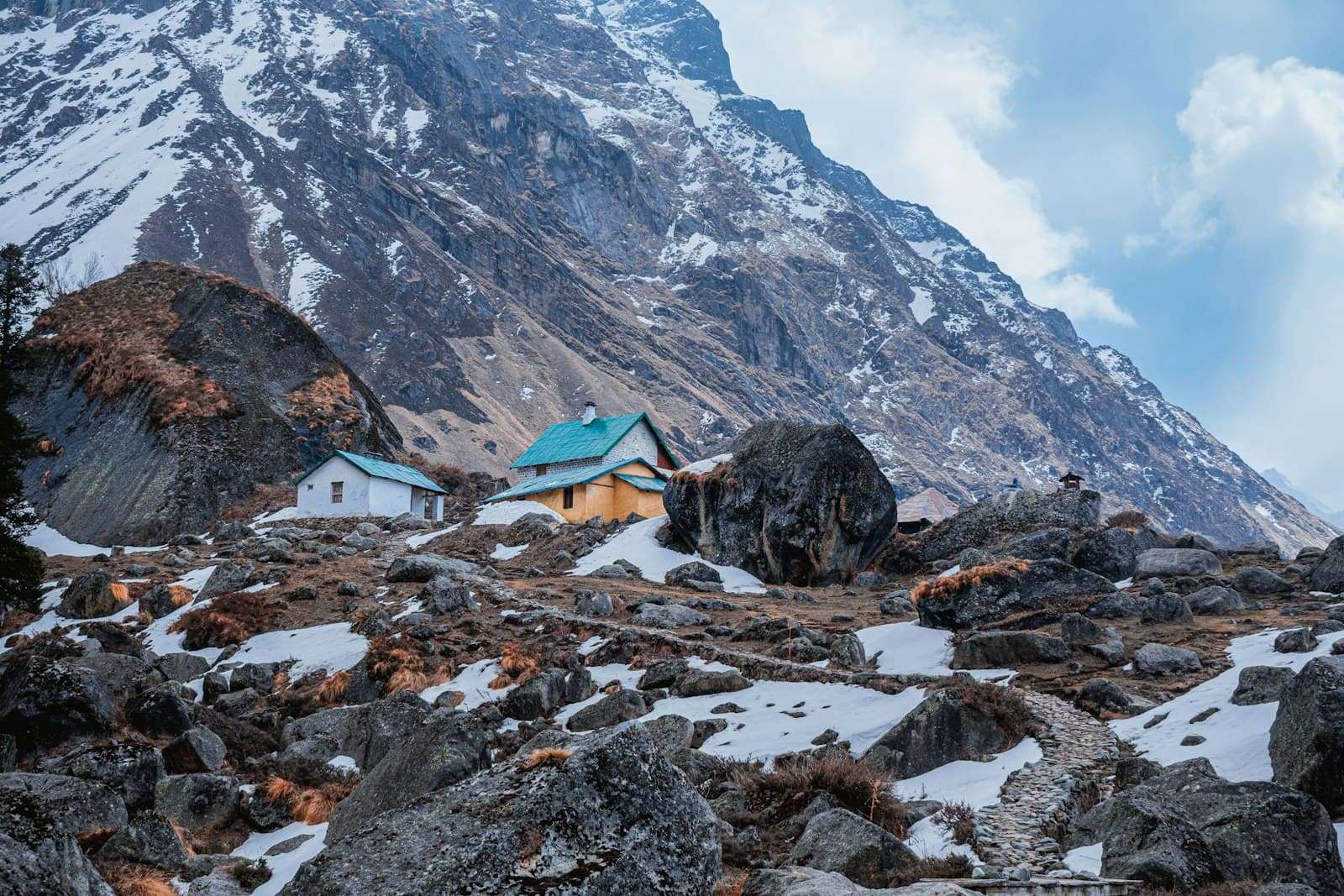 Two small cottages on a hillside below a snow-covered mountain
