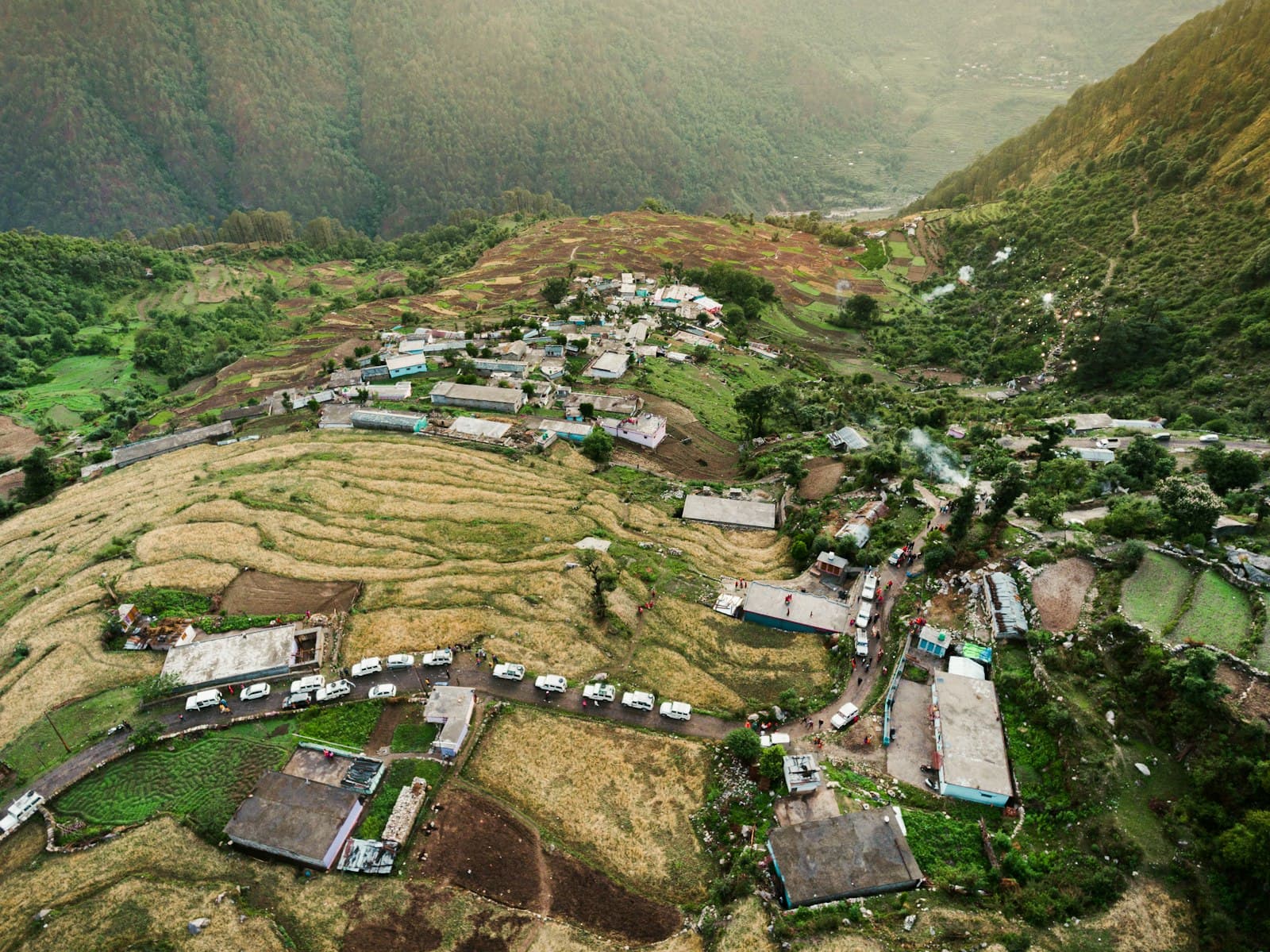 Aerial view of a hill village with terraced fields, a winding road and houses on a ridge above a deep valley
