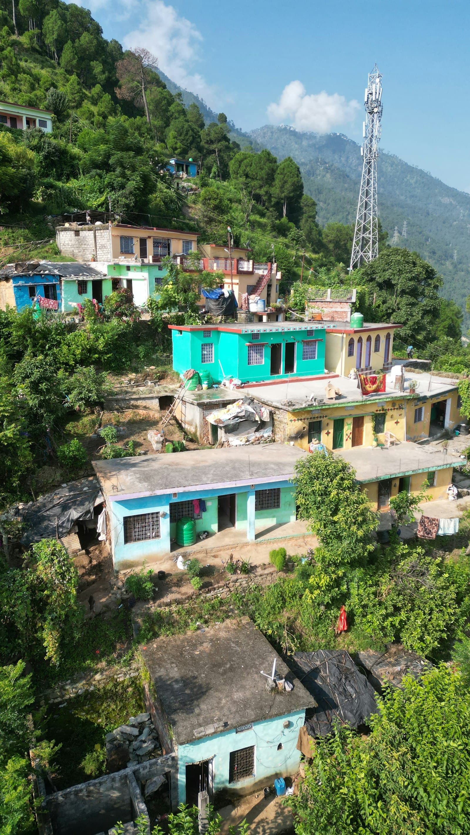 Row of painted concrete houses stepping down a green hillside, with a mobile tower on the ridge above
